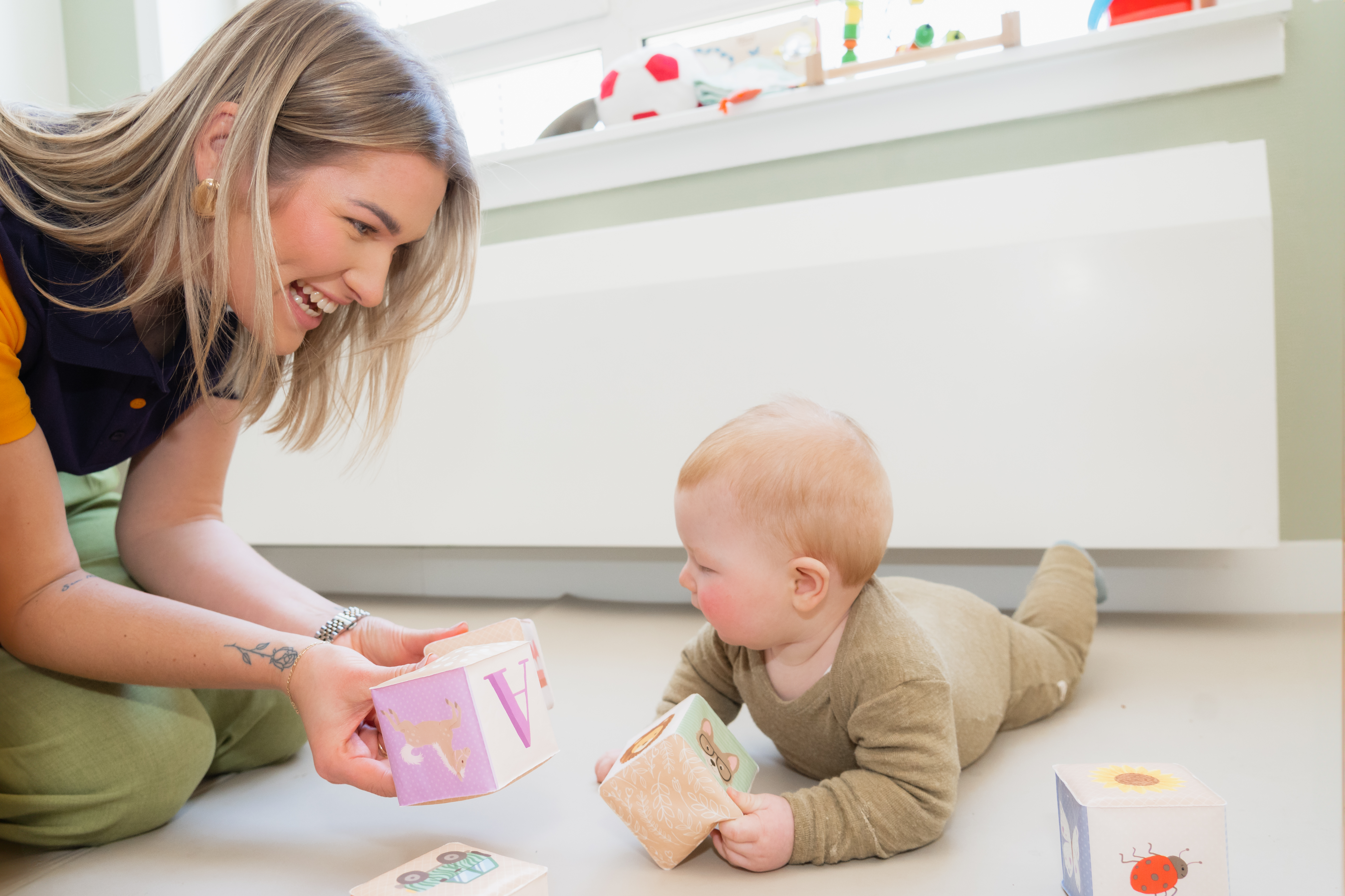 Een pedagogisch medewerker speelt met een baby die over de grond kruipt op een ouder-kindgroep van gro-up