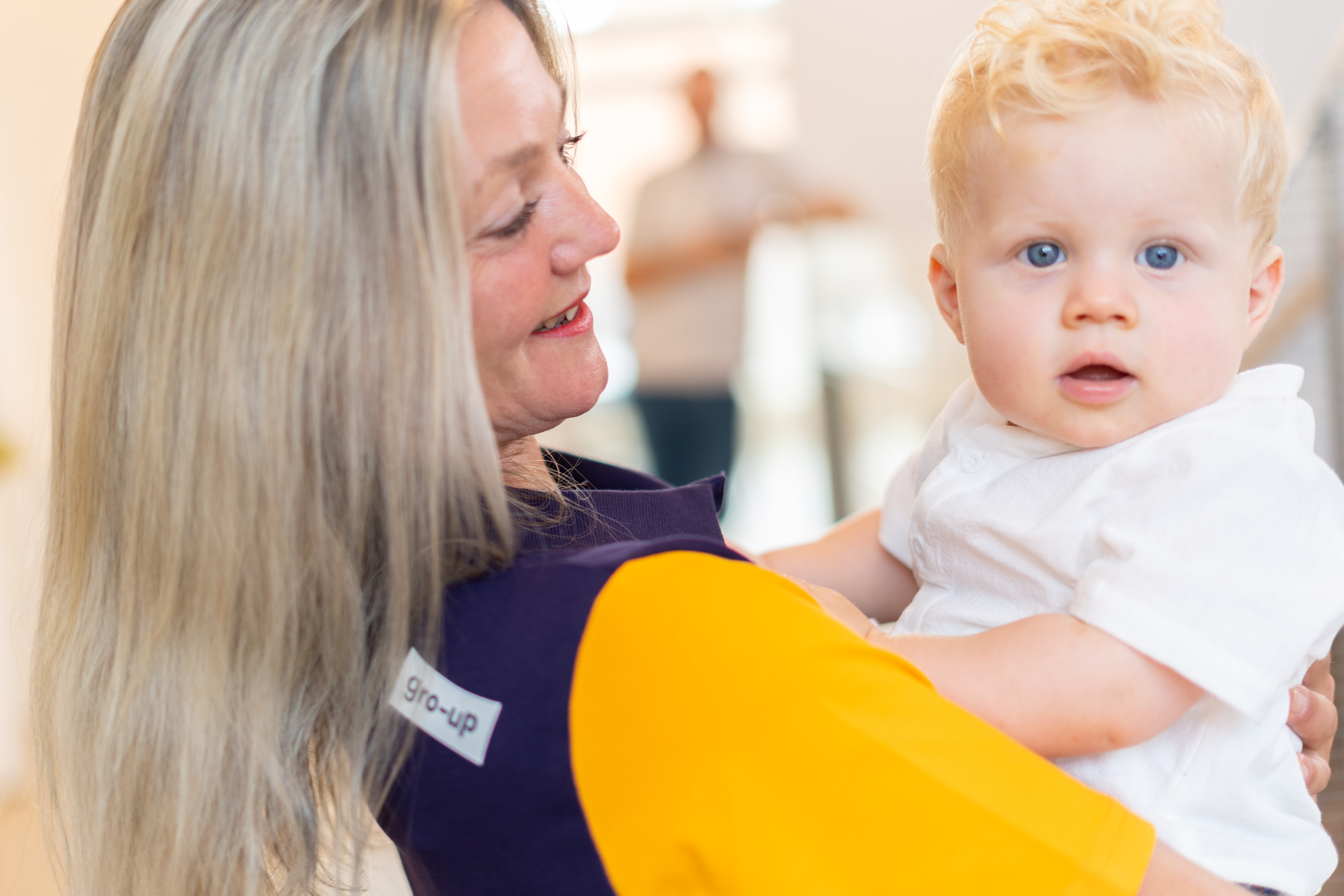 Baby met blond haar wordt vastgehouden door pedagogisch professional op kinderdagverblijf van gro-up