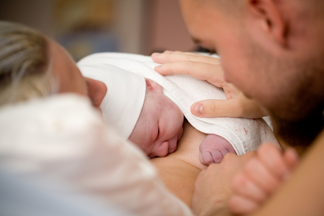 gro-up baby ligt op moeders borst en wordt geaaid door vader