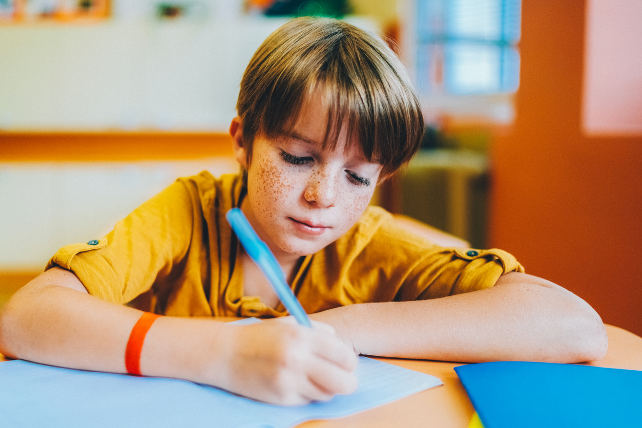 Schoolkind schrijft op een blauw gekleurd papier op de BSO plusopvang van gro-up