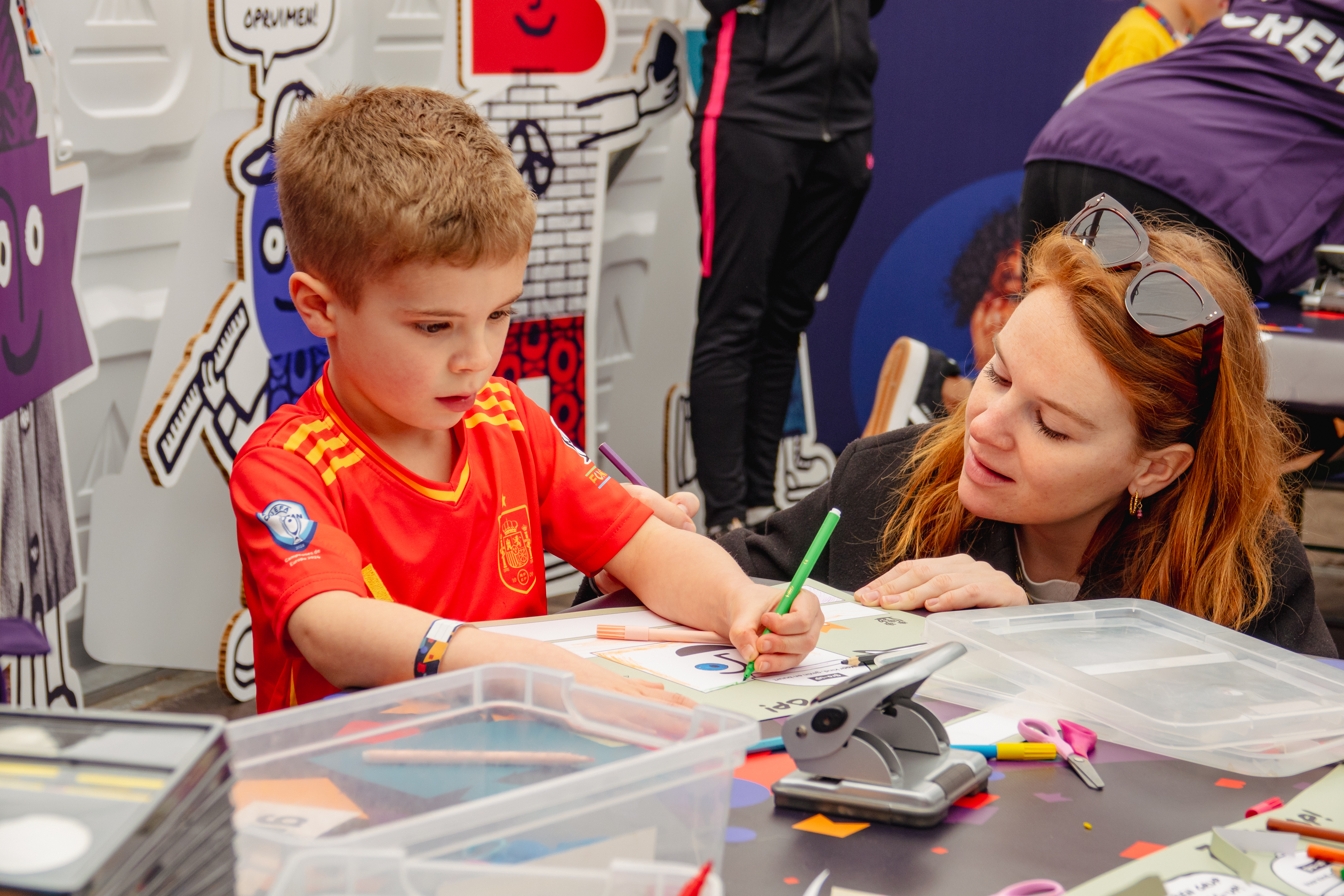 Een jongen tekent terwijl zijn moeder toekijkt in de kids corner tijdens de gro-up Jeugdlopen van de CPC Loop Den Haag