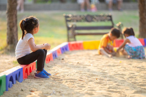 gro-up kind in zandbak kijkt naar spelende kinderen