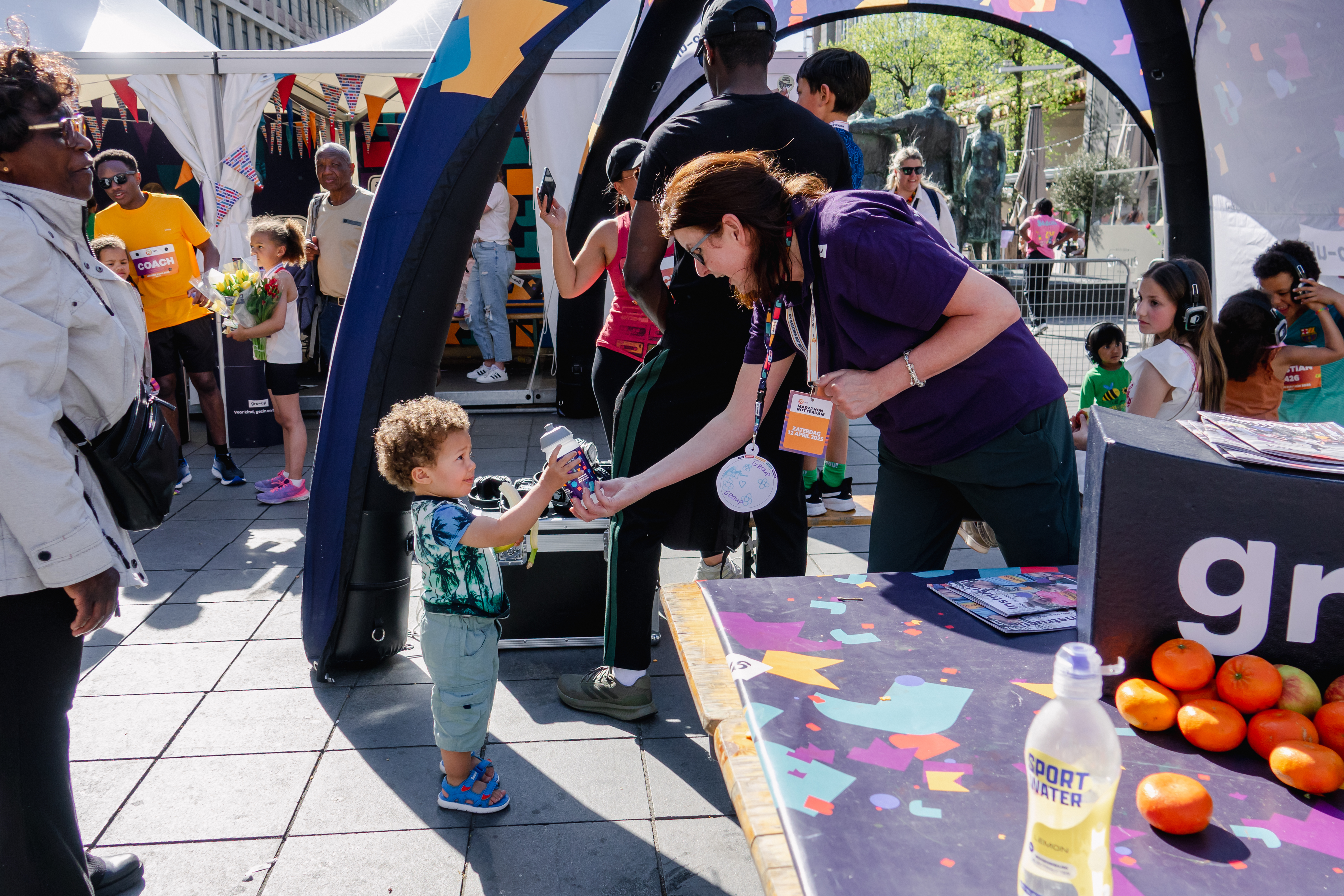 Een jongetje krijgt een bidon van een pedagogisch medeweker in de kids corner van gro-up tijdens de NN Kids Run van de Marathon Rotterdam