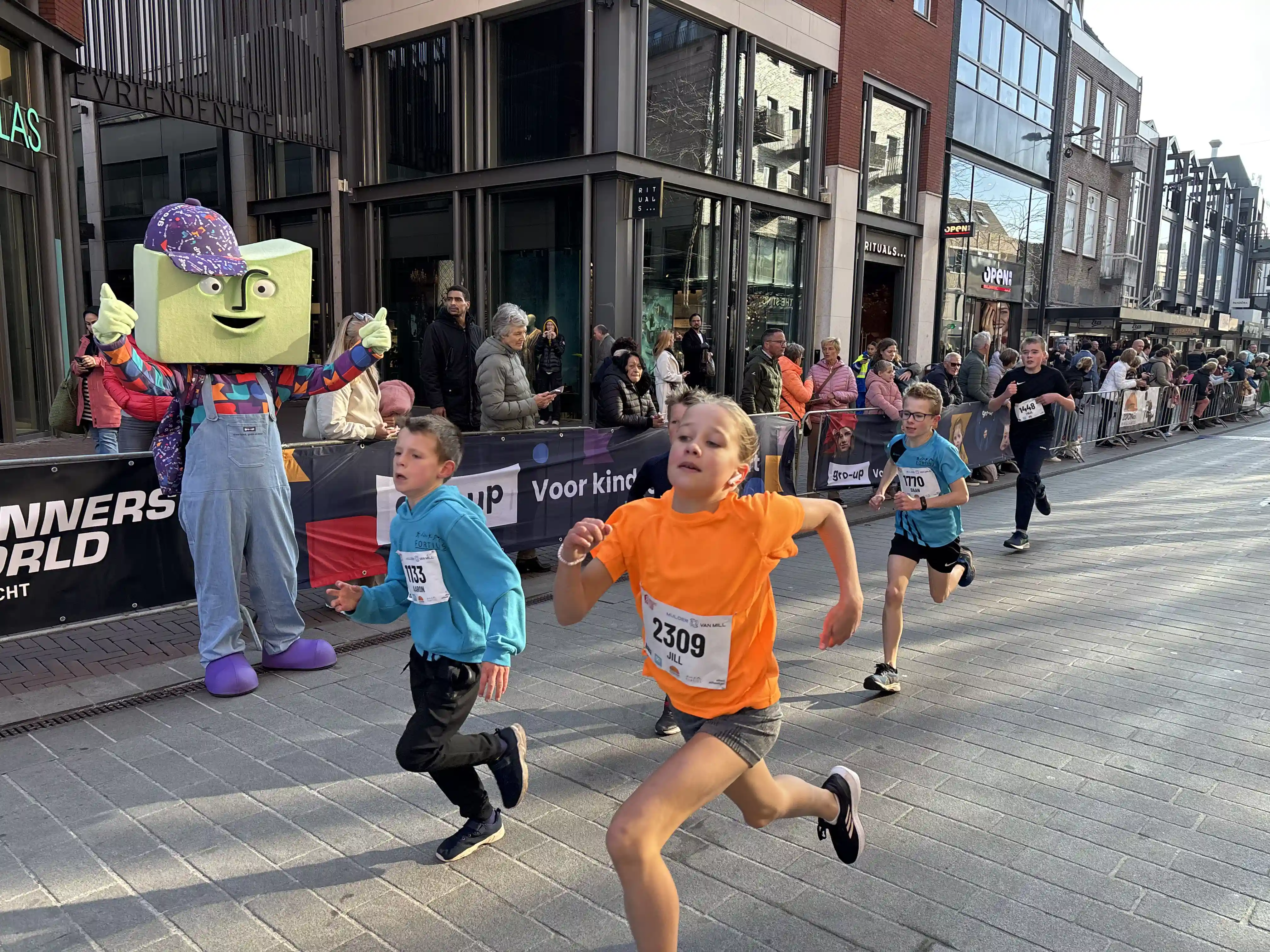 Kinderen rennen aangemoedigd door mascotte grup door het centrum van Dordrecht tijdens de DrechtStadLoop