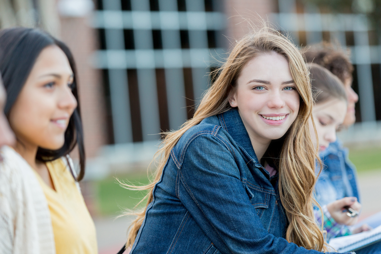 Blond meisje lacht in de camera, ze zitten tussen een groep meiden