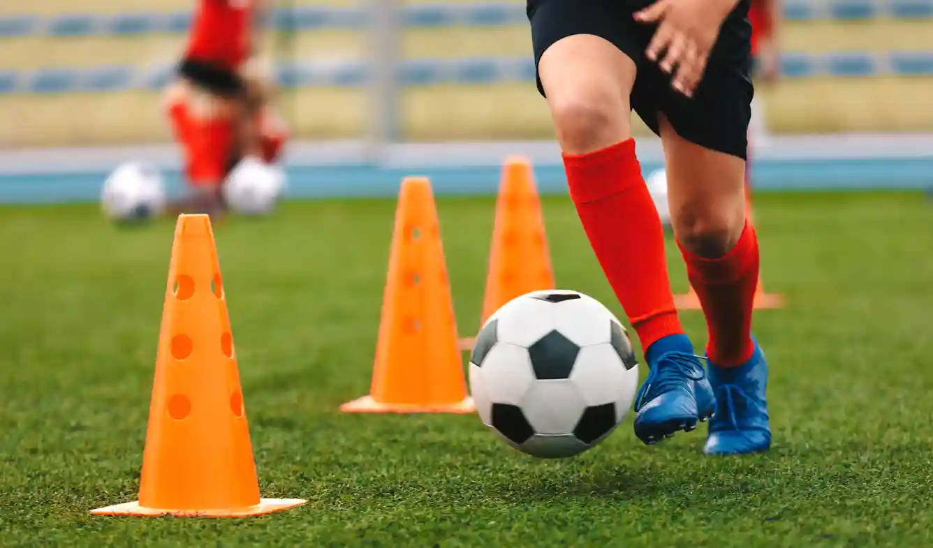 Een kind dribbelt met een voetbal lang pionnen op een voetbalveld