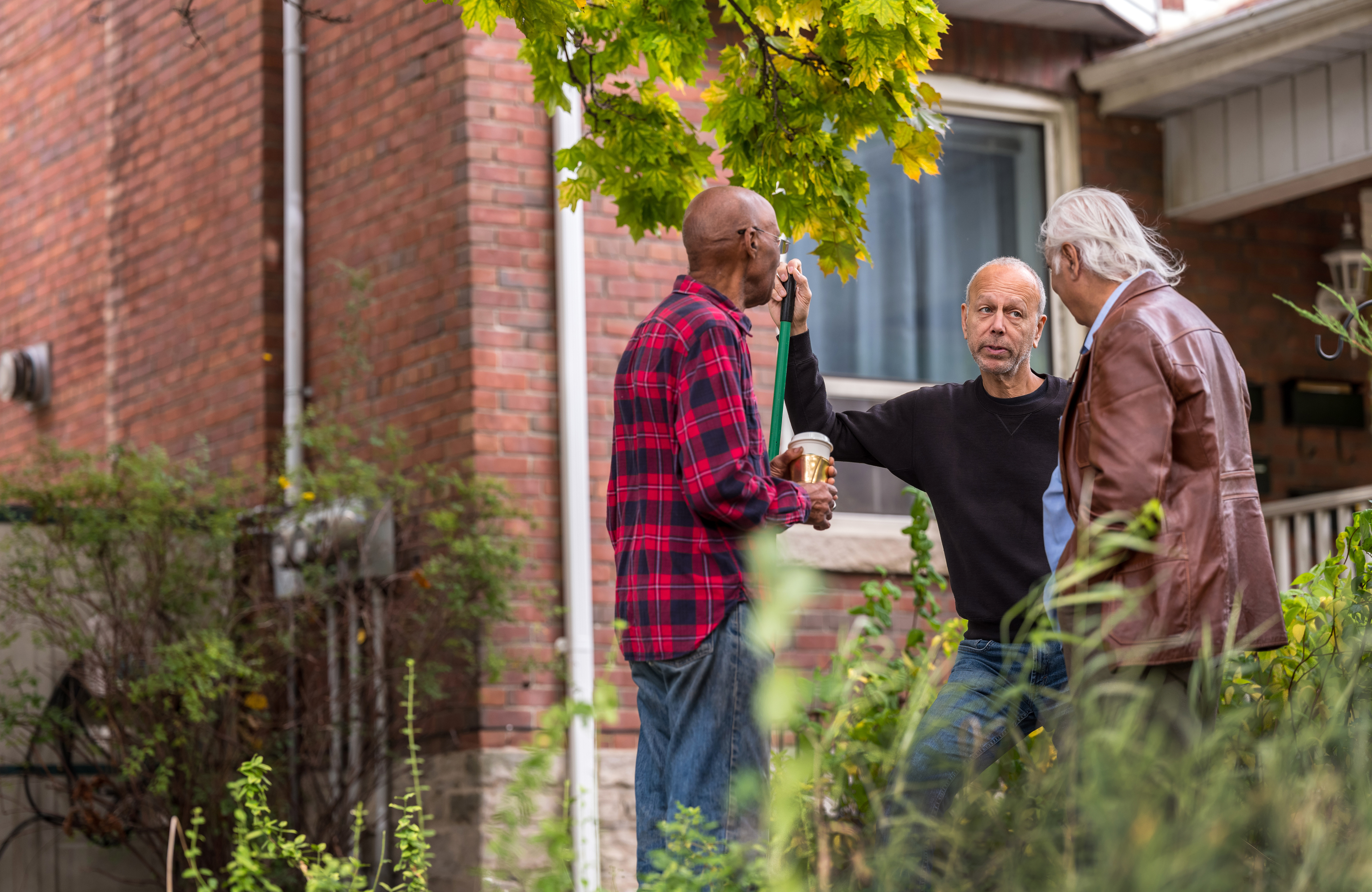 Drie buurmannen praten met elkaar in een tuin