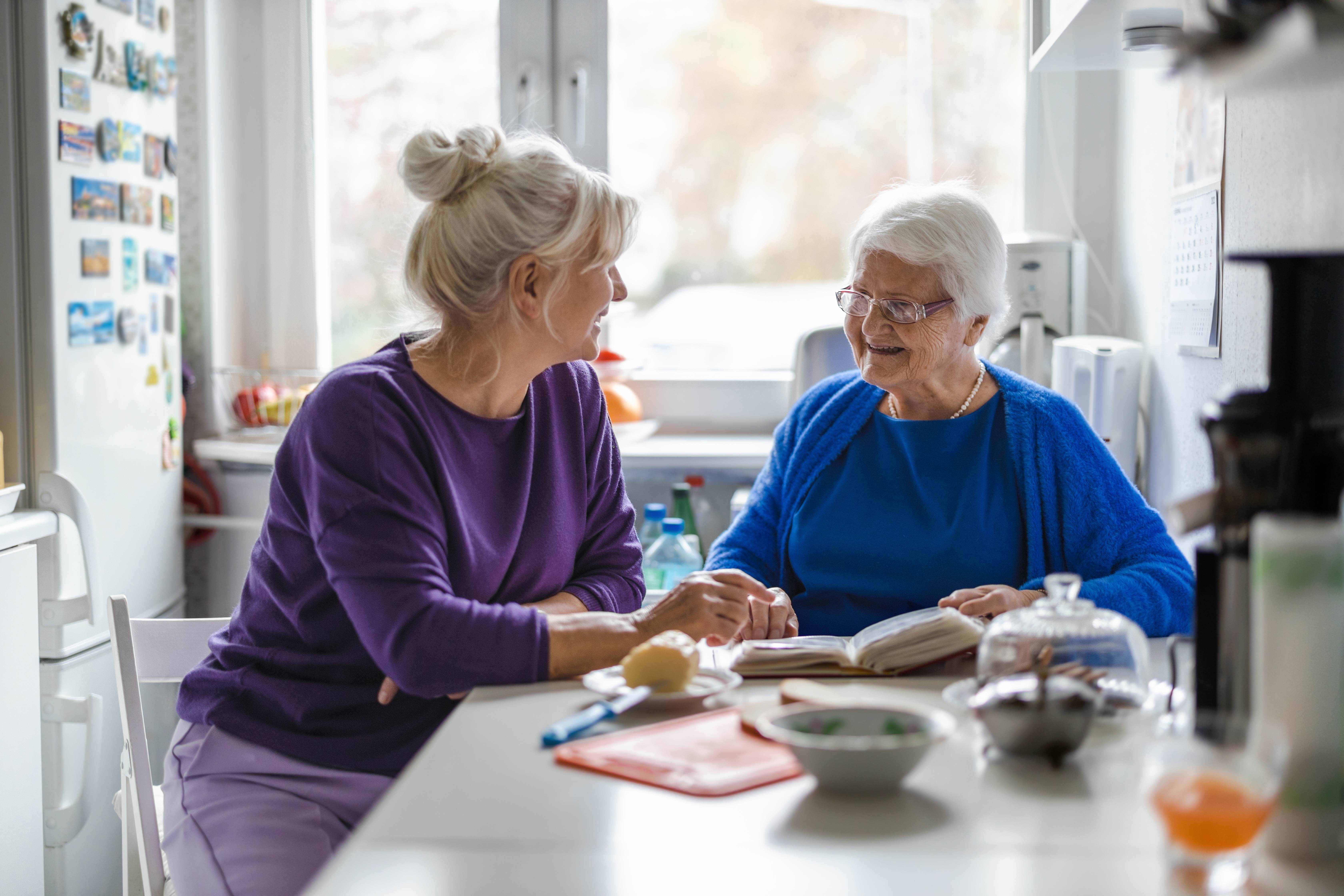 Een dame helpt een oudere dame met lezen en eten