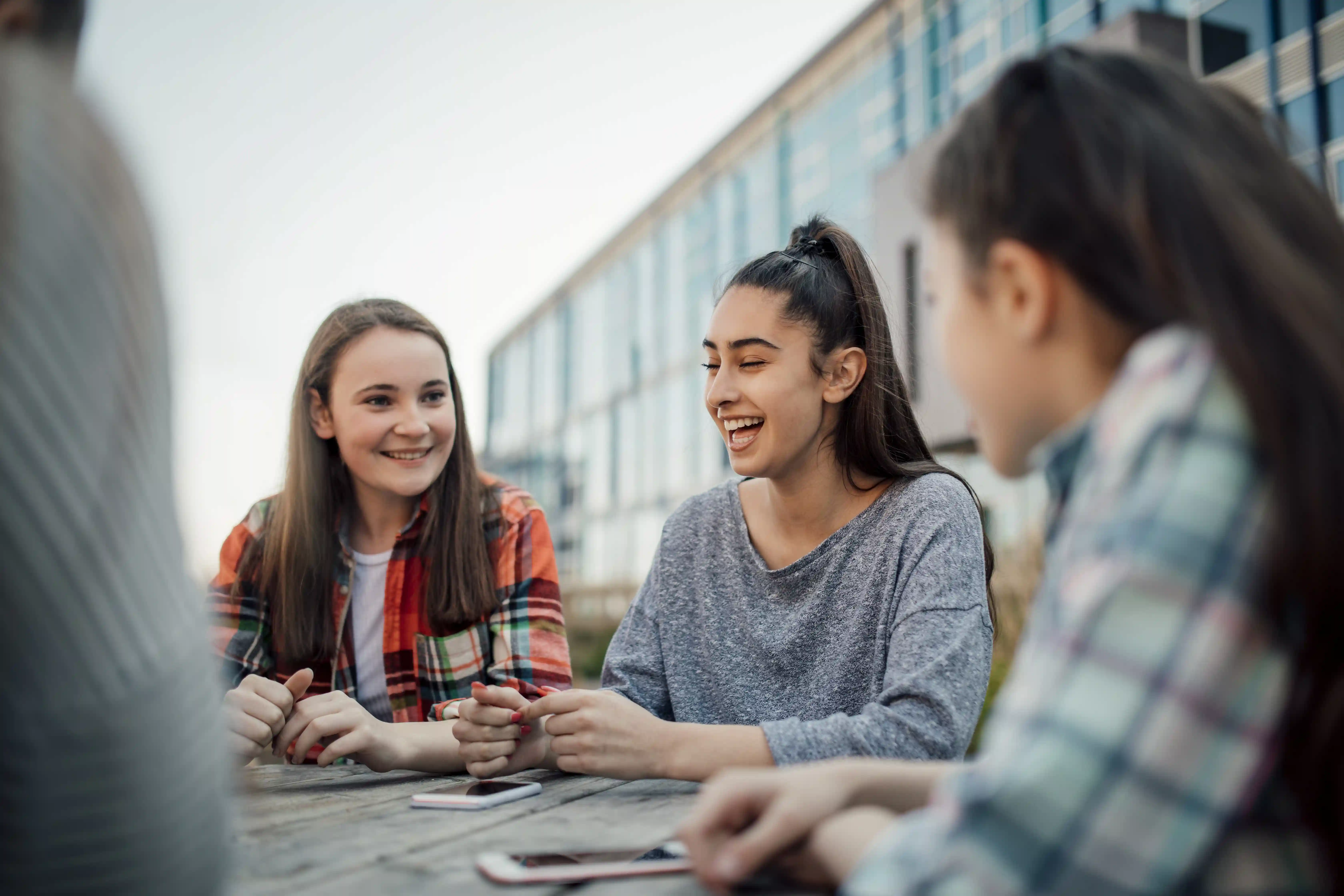 Drie jongere/adolescent meisjes lachend aan tafel voor school
