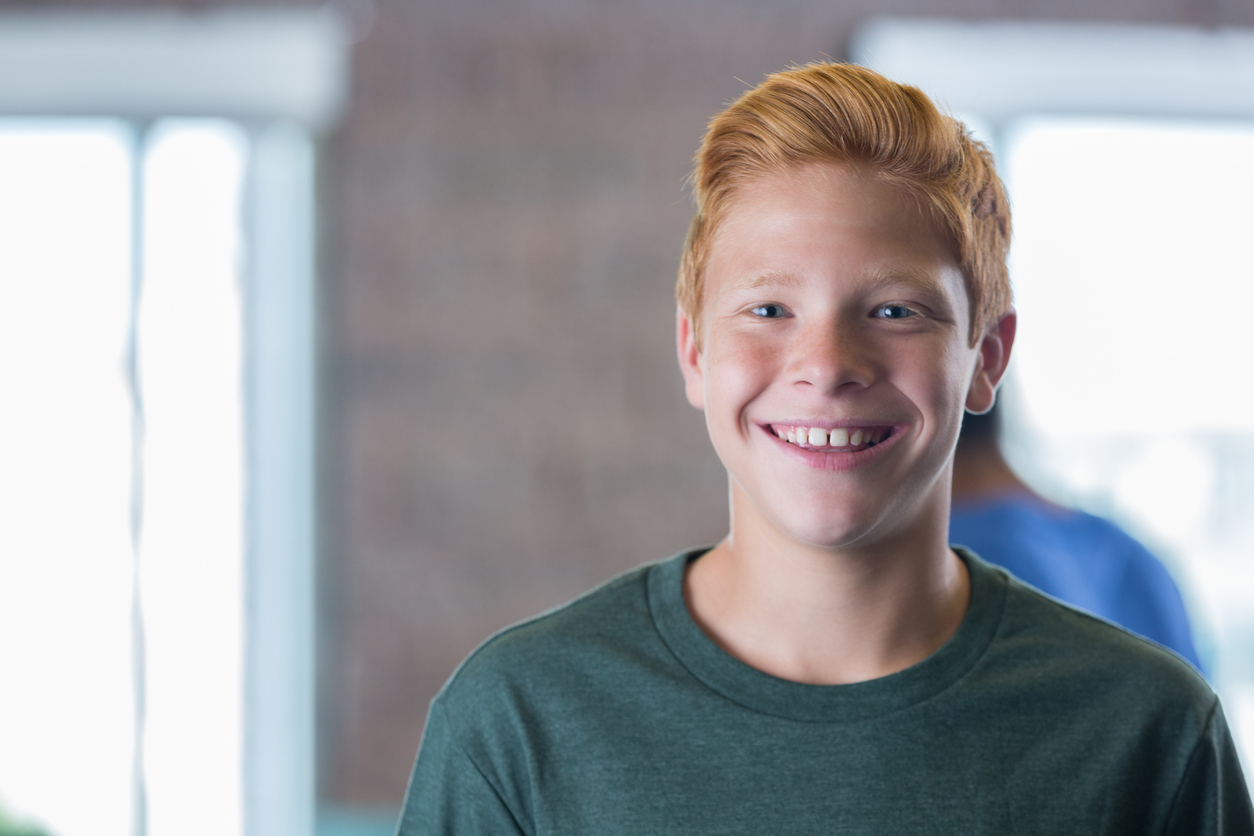 Rossige jongen kijkt lachend in de camera op school